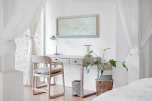 habitación de tonalidades claras con escritorio-tocador y planta